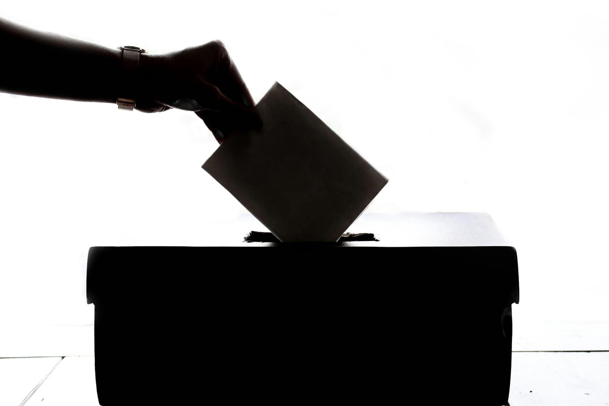 A hand in silhouette drops a ballot into a ballot box