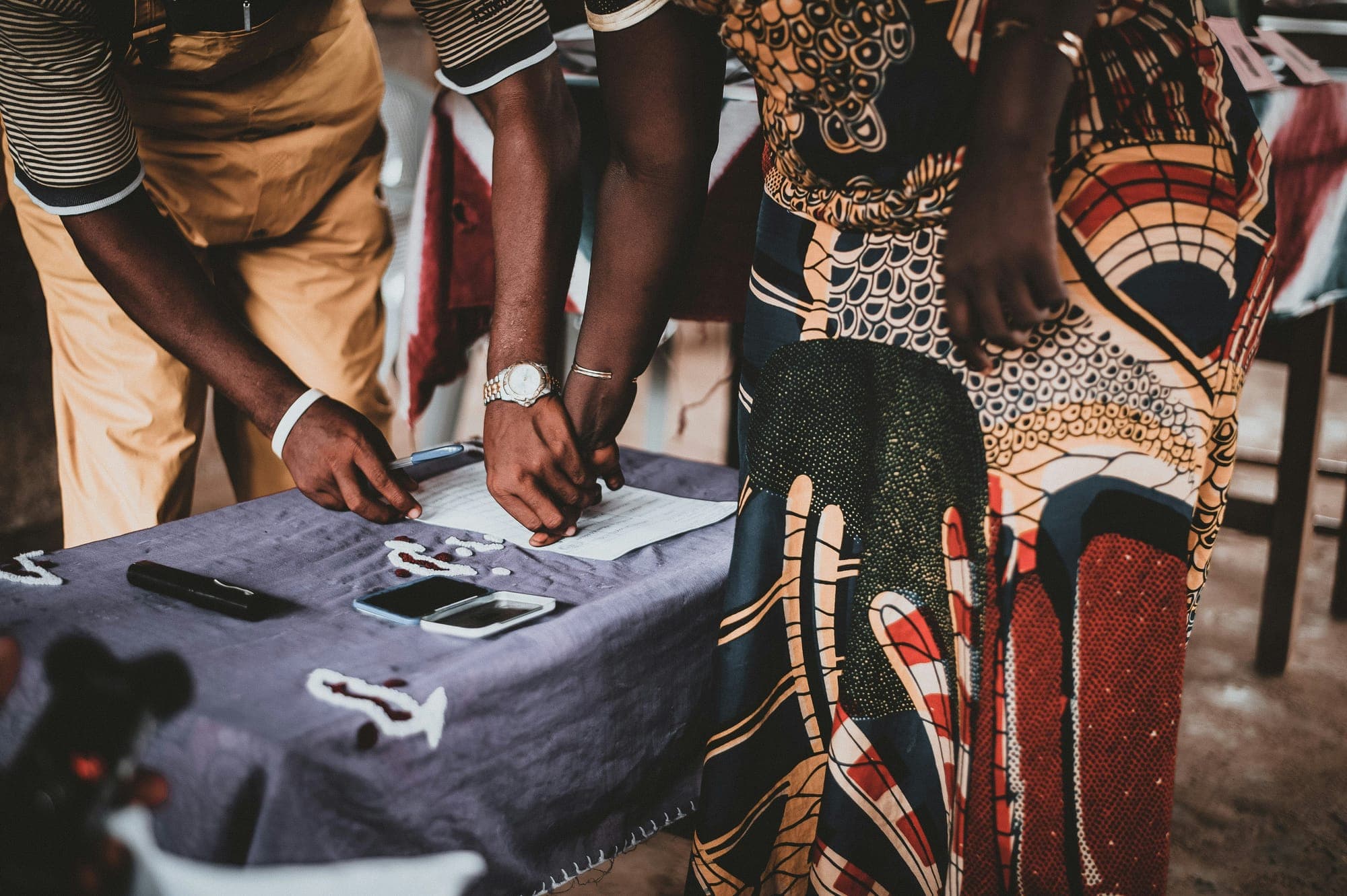 Hands filling in a registration form at a table draped in African print